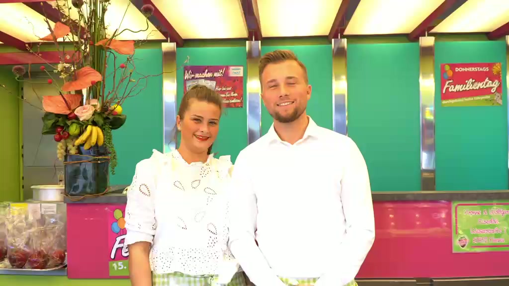 Schaustellerwagen Himmlische Früchte der Familie Eiserloh bei Nacht – pink-grünes Neonschild mit Schokofrüchten, Liebesäpfeln und Fruchtauslage